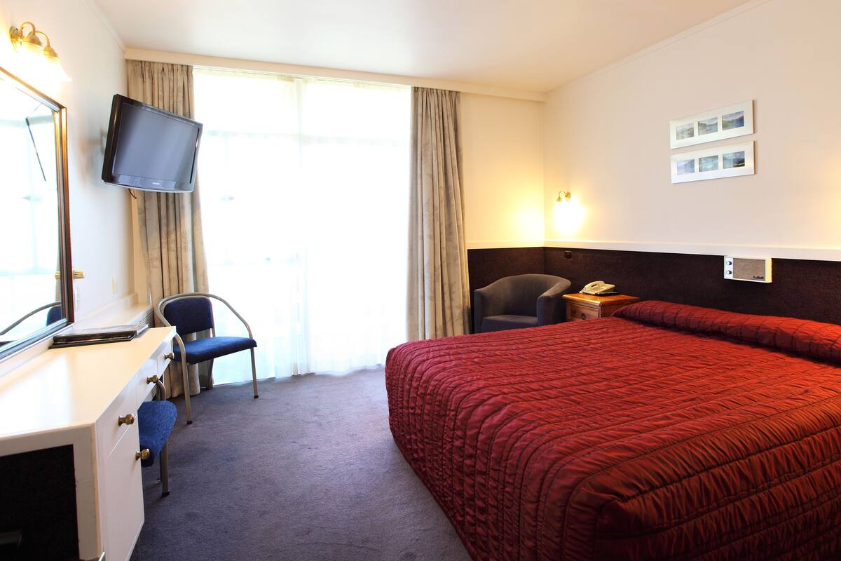 A hotel room with a bed, a desk, a chair, a television, and a window with curtains.
