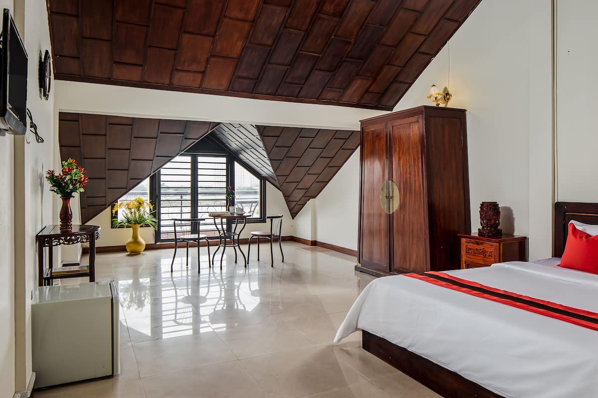 Ein Schlafzimmer mit einem großen Bett, einem Holzschrank, einem Esstisch mit Stühlen und Blick durch ein Fenster.