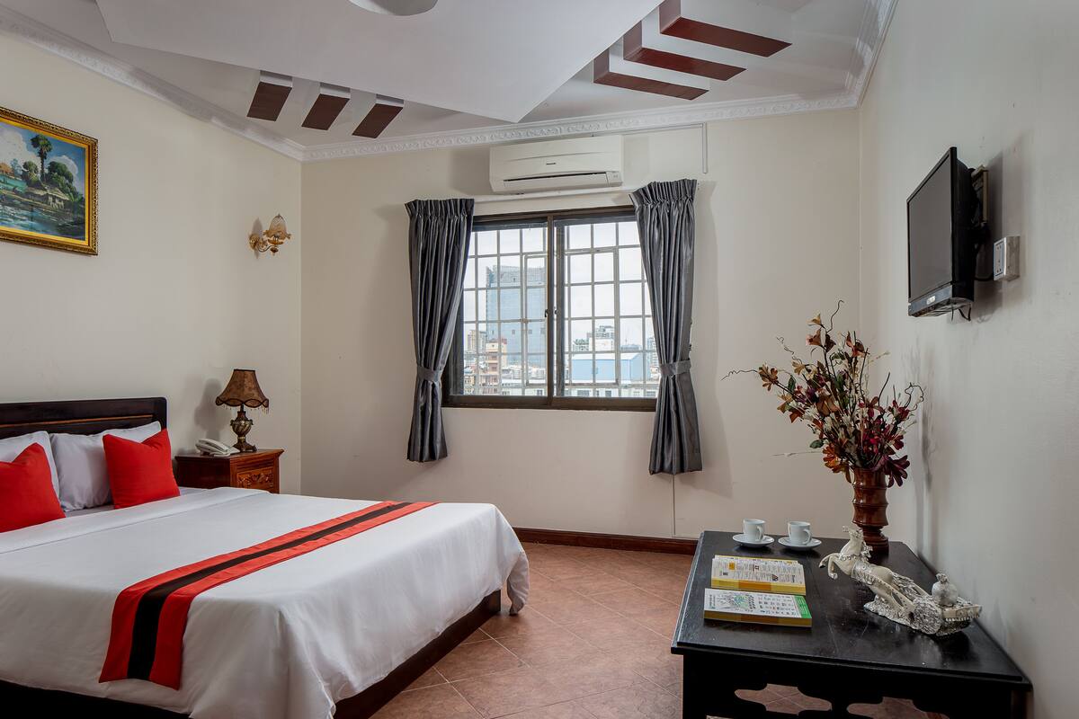 Ein Hotelzimmer mit einem Bett, einem Schreibtisch mit einer Vase, einem Fernseher und einem Fenster mit Vorhängen.