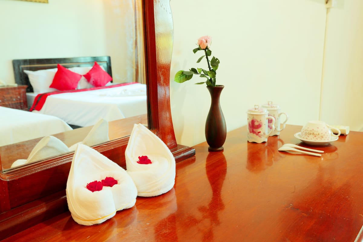 Ein Hotelzimmer mit einem ordentlich bezogenen Bett, einer Vase mit einer einzelnen Rose, einem Tee-Set und einem Spiegel, der den Raum widerspiegelt.