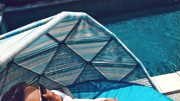 A person reclining on a blue lounge chair by a pool with two plates of food on the ground beside them. - La Belle Villa (Seminyak)