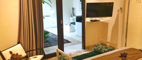 A hotel room with a bed, a chair, a television, and a view of the outdoor area.