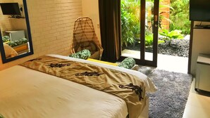 A bedroom with a bed, a chair, a television, and a view of a garden through a sliding door. - La Belle Villa (Seminyak)