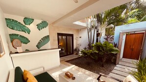 A modern interior with a reception desk, a seating area with a sofa and armchair, and a garden with tropical plants. - La Belle Villa (Seminyak)