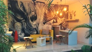A modern living room with a large abstract painting, a yellow sofa, a coffee table, and a small kitchen area with a counter and hanging lights. - La Belle Villa (Seminyak)
