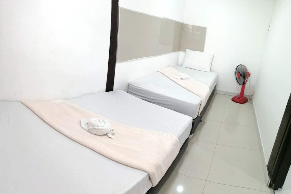 Une chambre d’hôtel avec deux lits, une fenêtre avec des rideaux, une table de chevet et un ventilateur rouge.