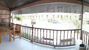 A covered balcony with wooden furniture, a view of the street, and a decorative lattice wall. - Baan Kaew Ruen Kwan (Pattaya)