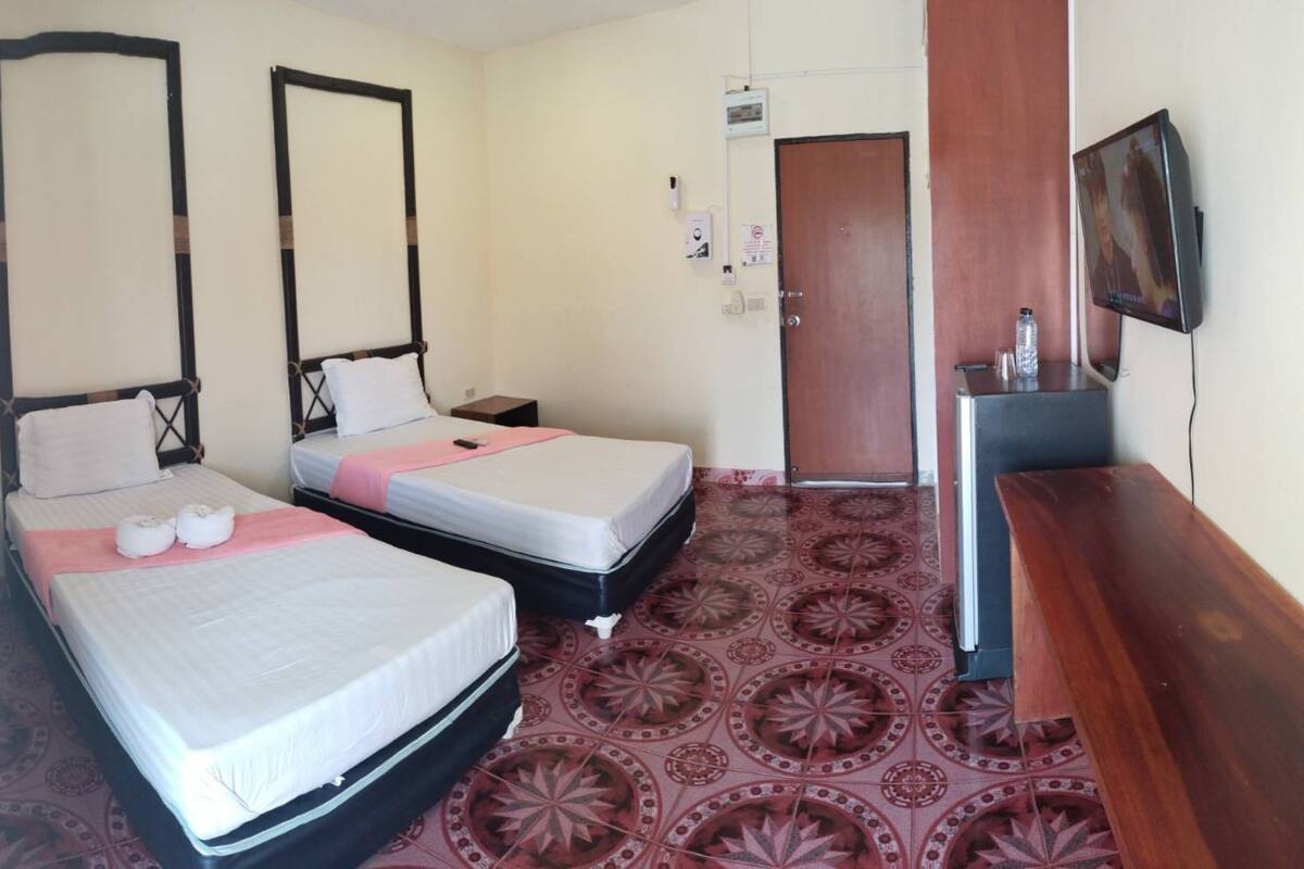 Une chambre d’hôtel avec deux lits, une commode en bois, une télévision et une moquette à motifs.