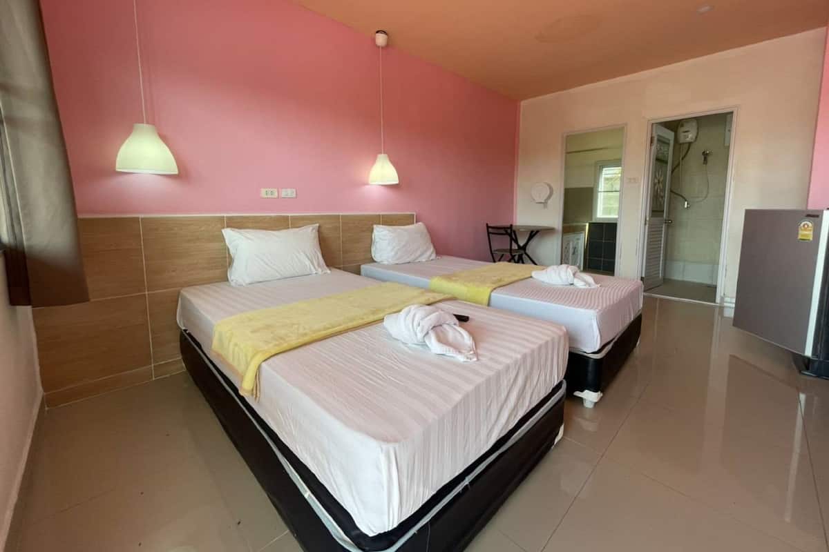 Une chambre d’hôtel avec deux lits, une petite table, un espace douche et un réfrigérateur.