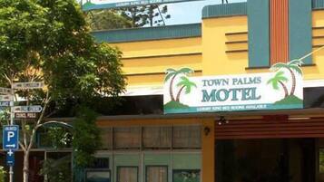 Un motel appelé « Town Palms », avec un panneau indicateur, un panneau de signalisation pour le stationnement et une personne assise à l’extérieur.