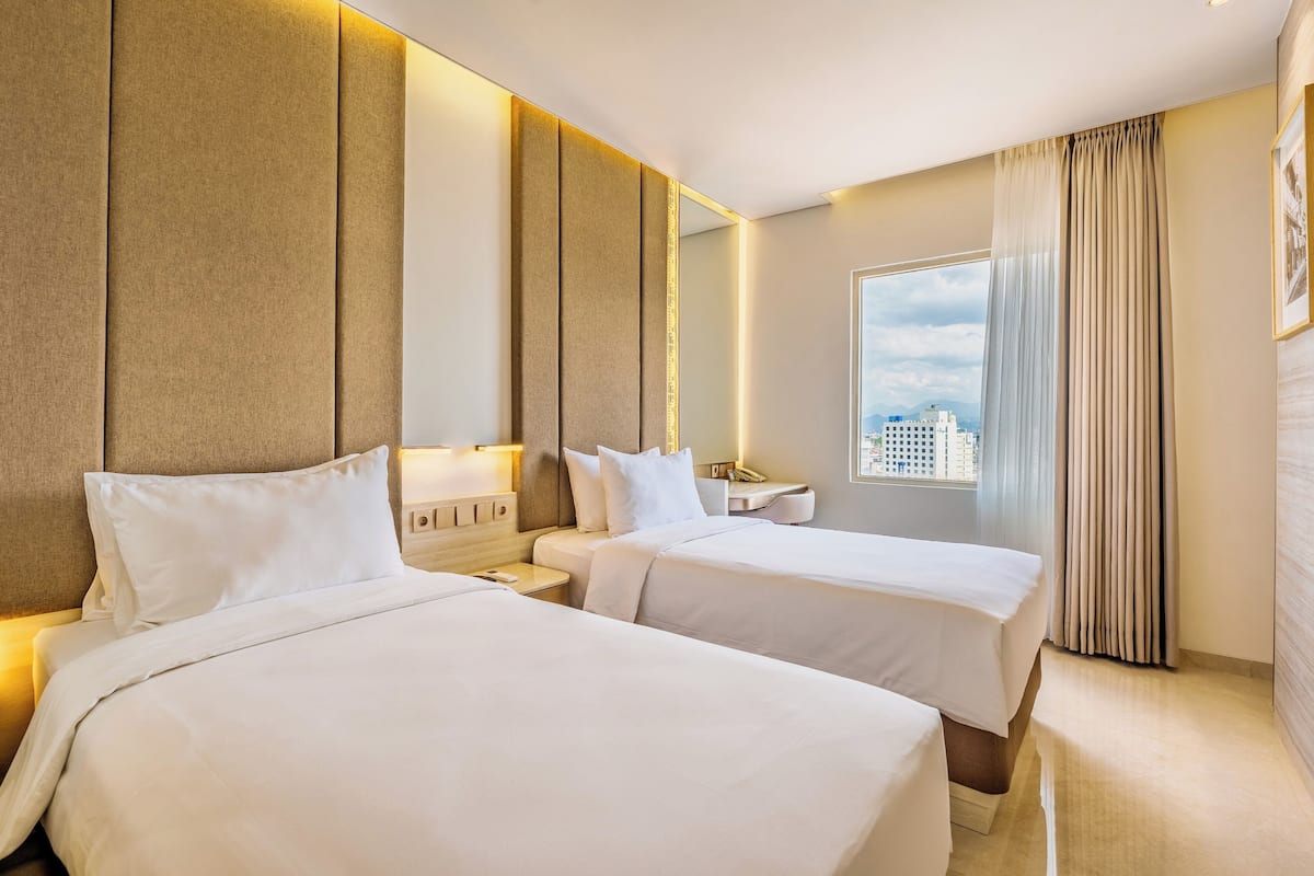 Habitación de hotel con dos camas, un ventanal grande y vista a la ciudad.