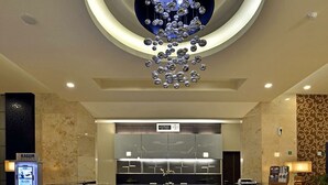 A modern hotel lobby with a marble floor, a central reception desk, and a unique circular ceiling light fixture.