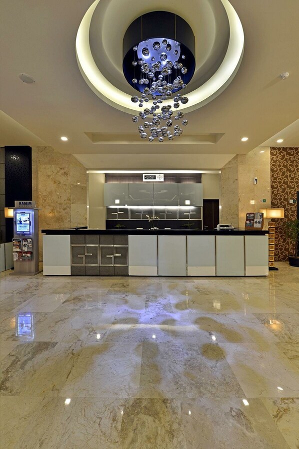 A modern hotel lobby with a marble floor, a central reception desk, and a unique circular ceiling light fixture. - Feruci Hotel (Bandung)