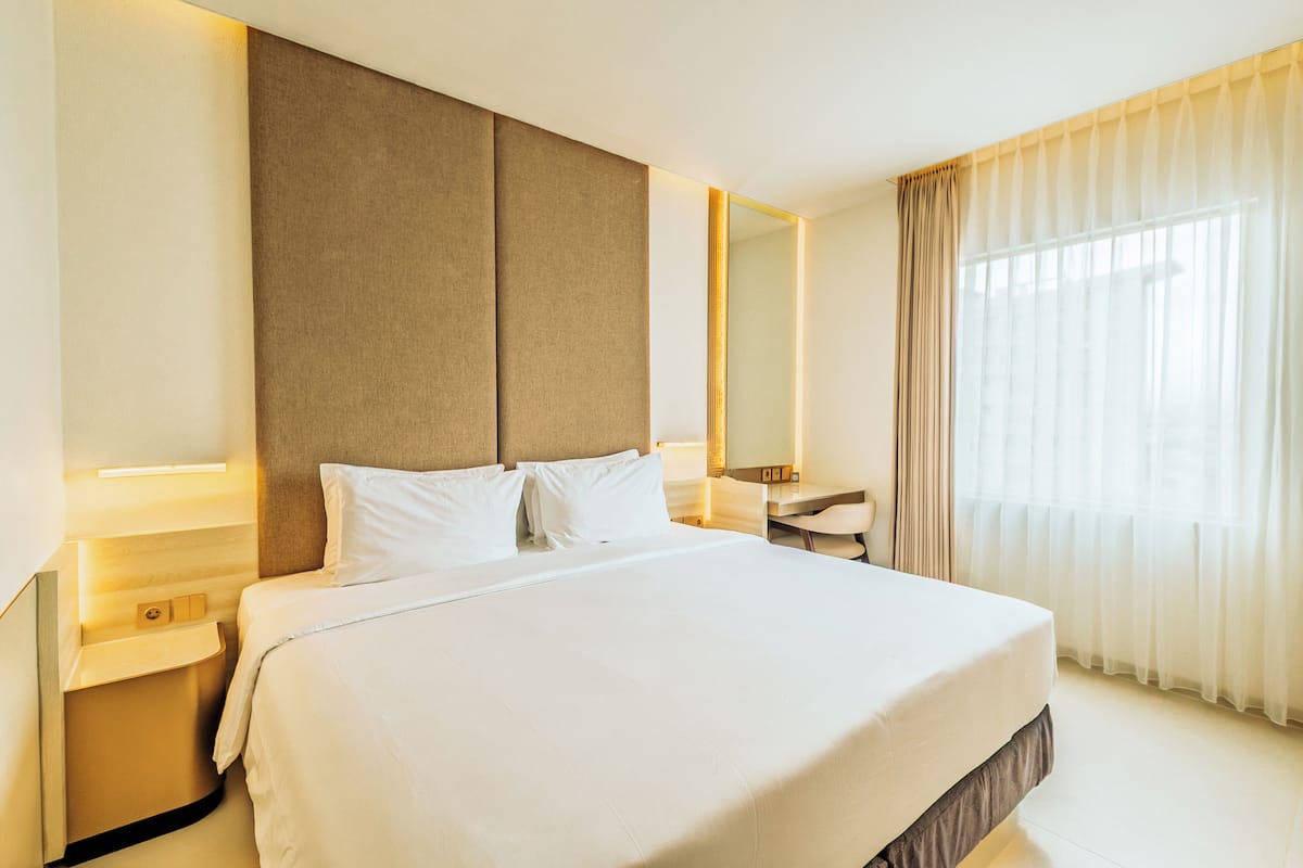 Una habitación de hotel con una cama grande, mesitas de noche, un escritorio y un espejo.