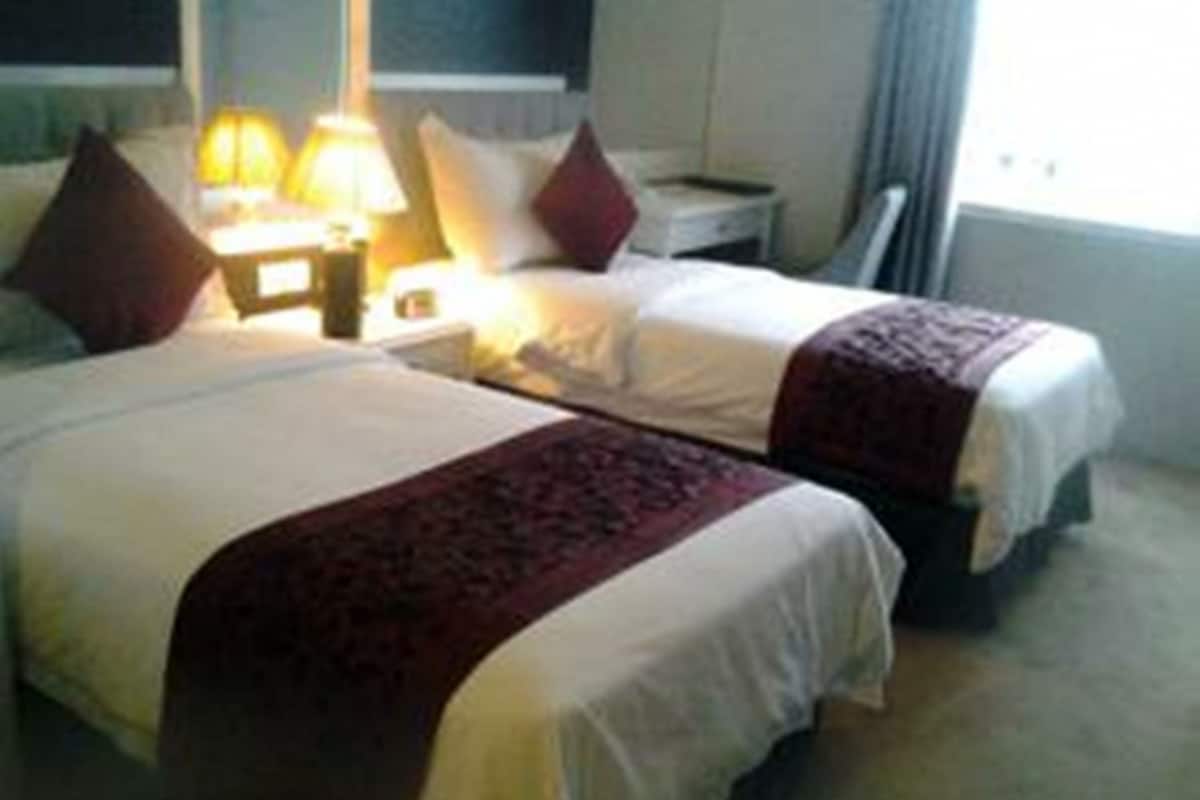 Una habitación de hotel con dos camas, una mesita de noche con lámpara y una ventana con cortinas.