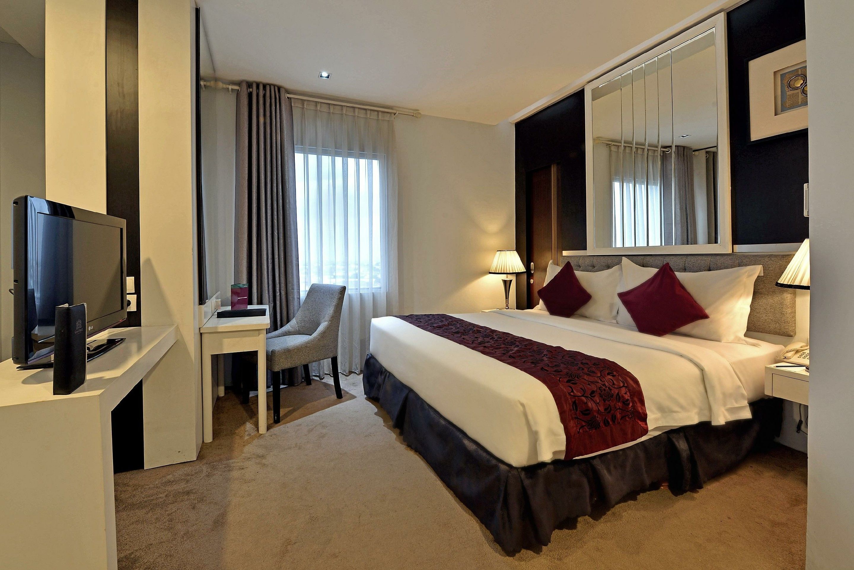 A hotel room with a bed, a desk, a chair, a television, and a large mirror.