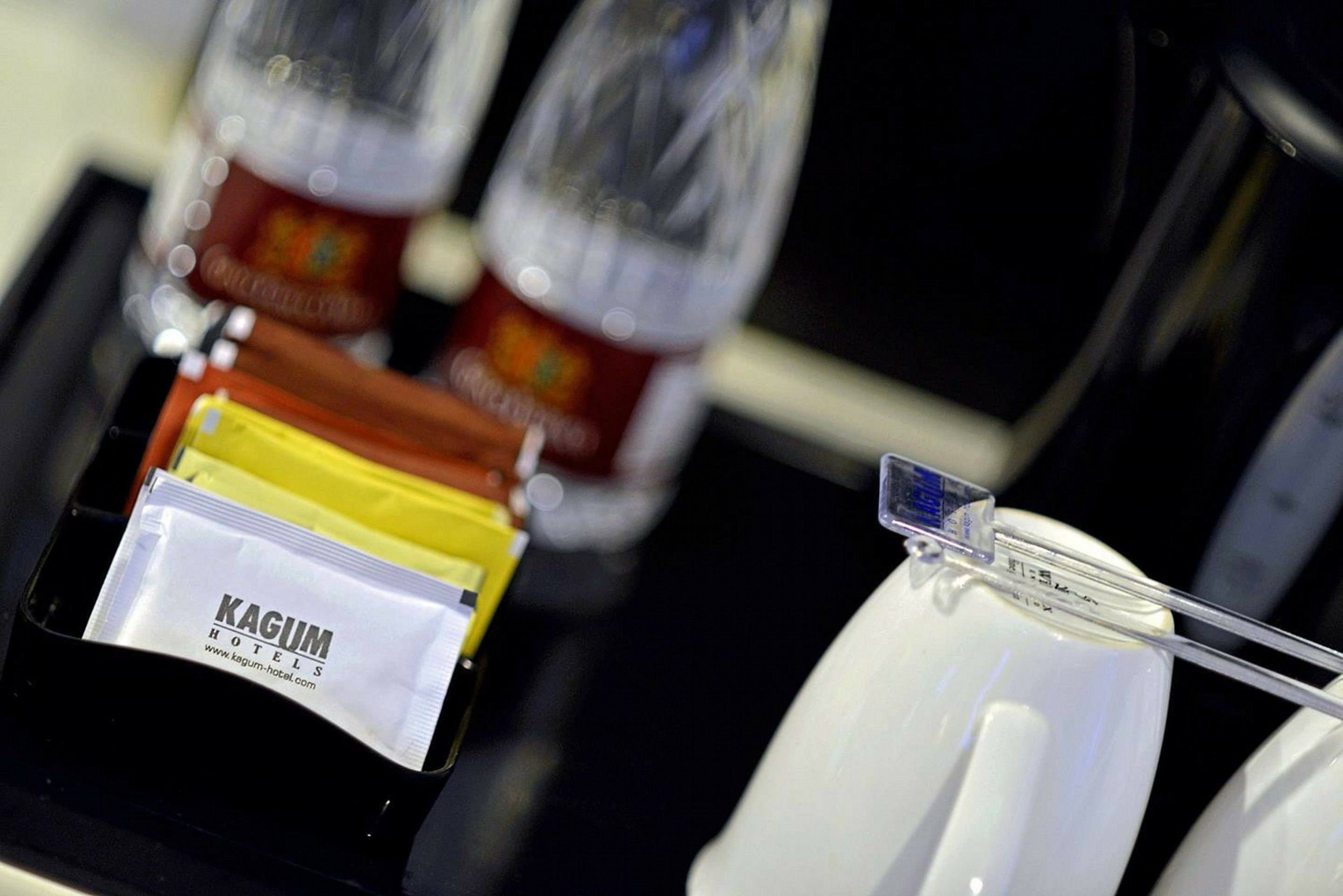 Un mini-bar d’hôtel comprenant une carte KAGUM, une bouteille d’eau et une bouteille de jus de fruits.