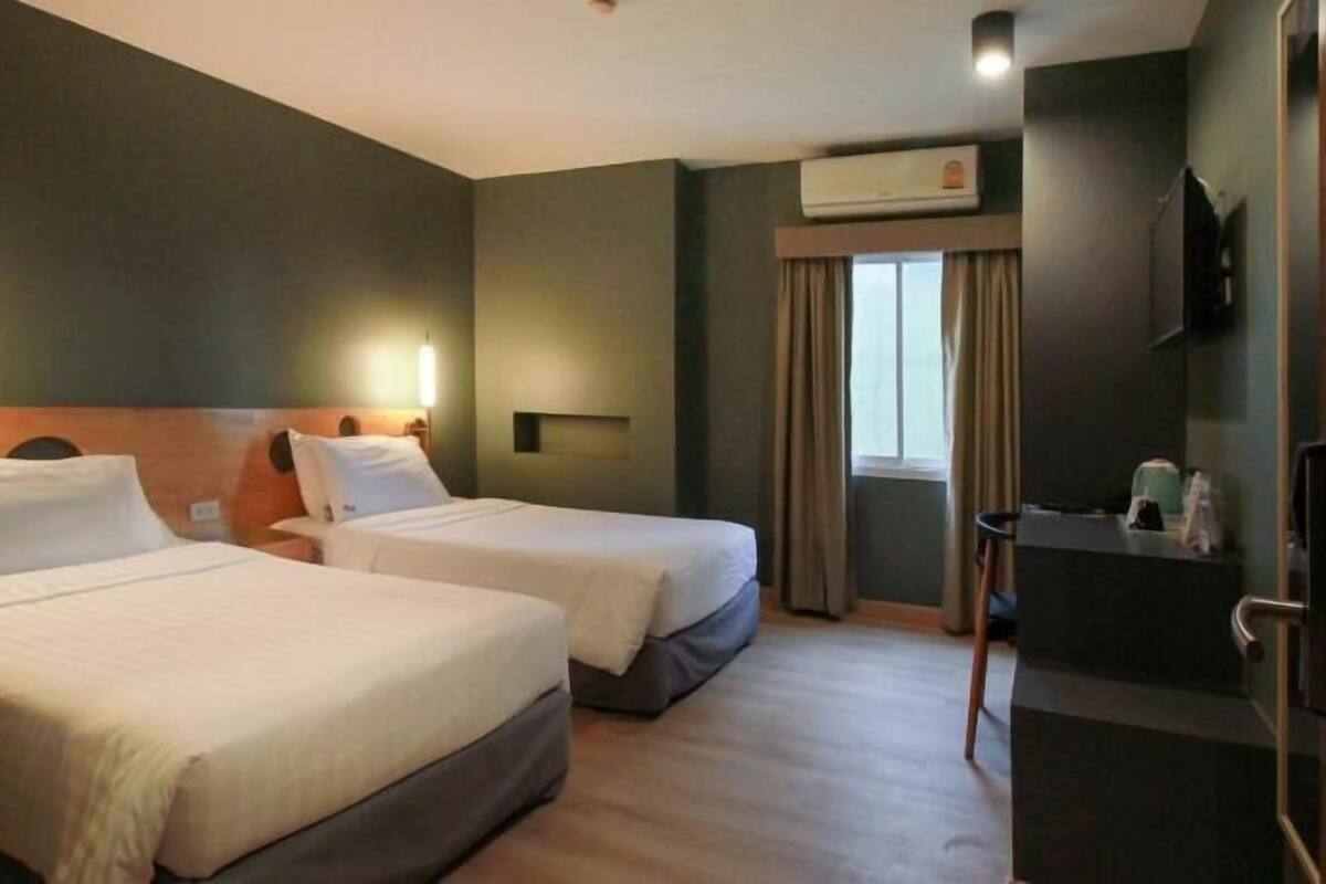 A hotel room with two beds, a desk, a chair, an air conditioning unit, and a television.