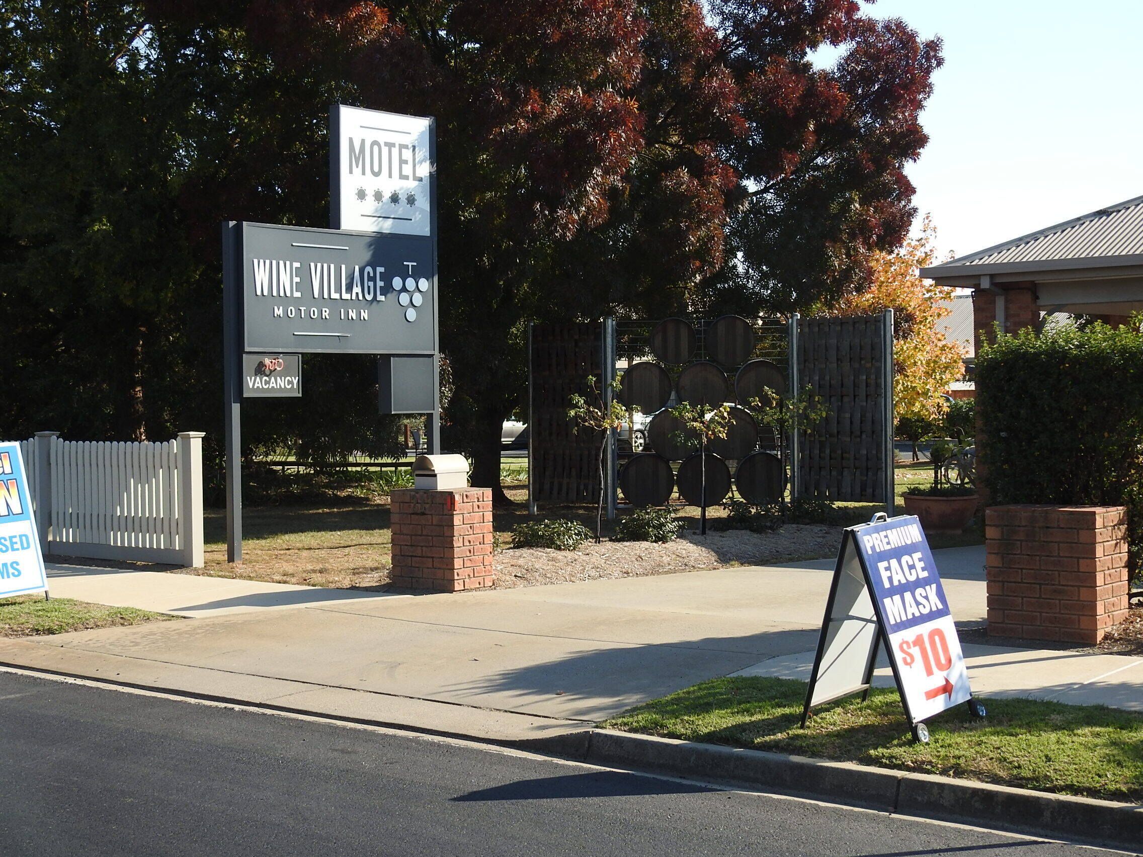 A motel sign with a wine village logo, a vacant sign, and a face mask sign.