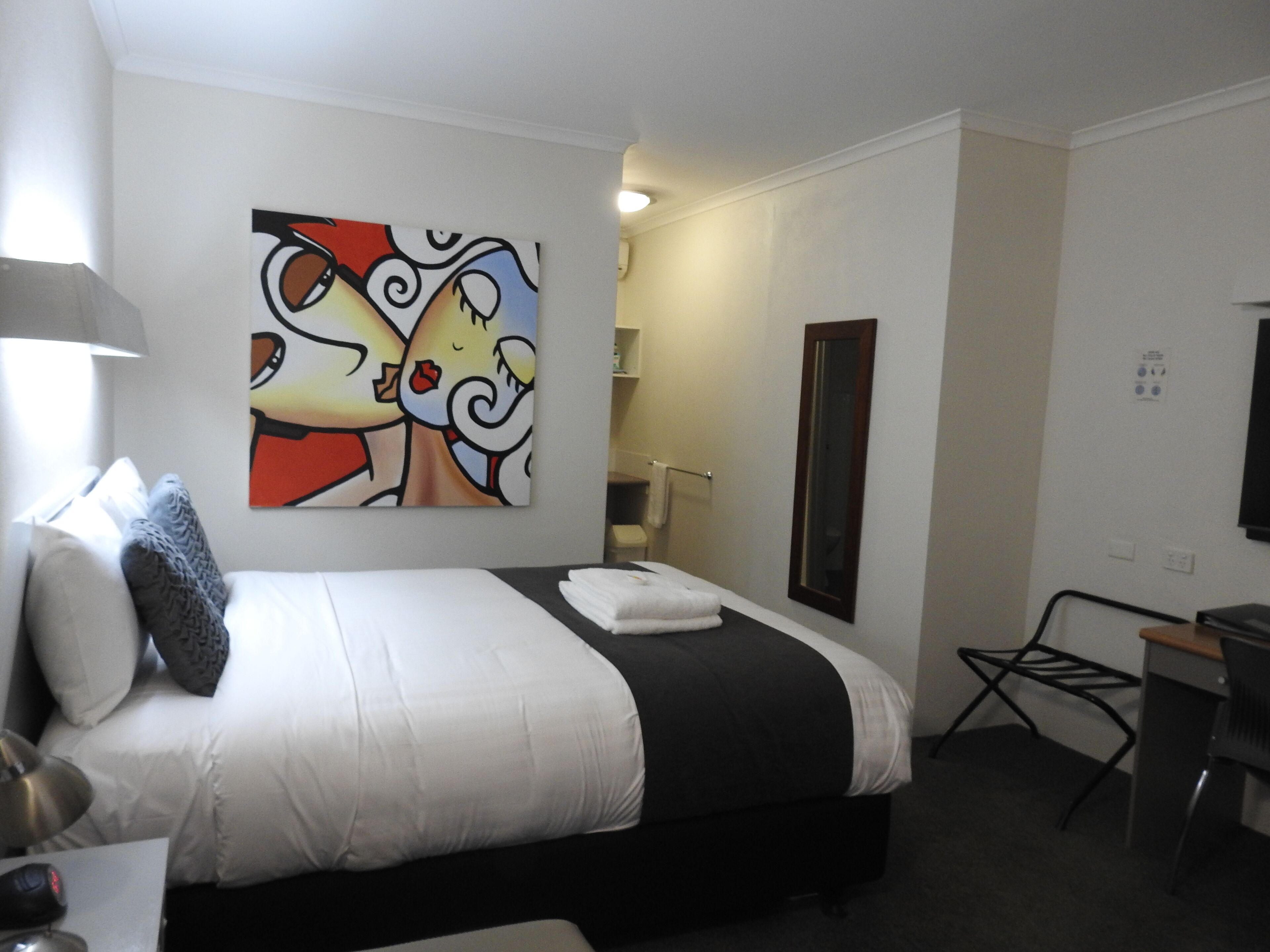Ein Hotelzimmer mit einem Bett, einem Schreibtisch, einem Sessel, einem Spiegel und einem Bild an der Wand.