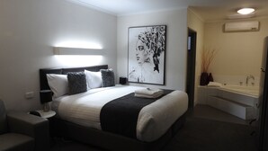 A modern hotel room with a large bed, bedside tables, a desk, and a bathroom with a sink and mirror. - Wine Village Motor Inn (Rutherglen)