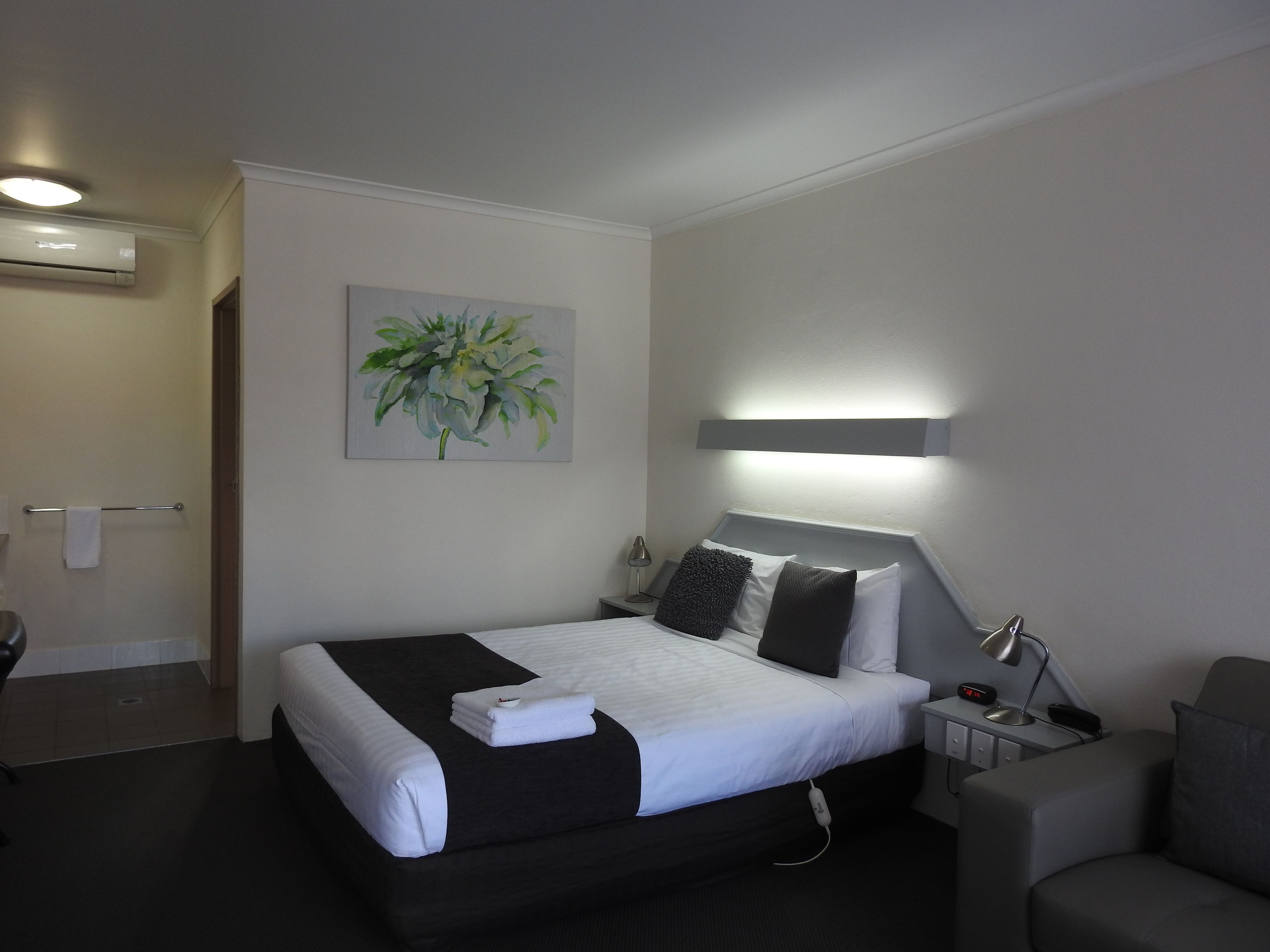 A hotel room with a bed, bedside tables, a lamp, a chair, and a painting on the wall.