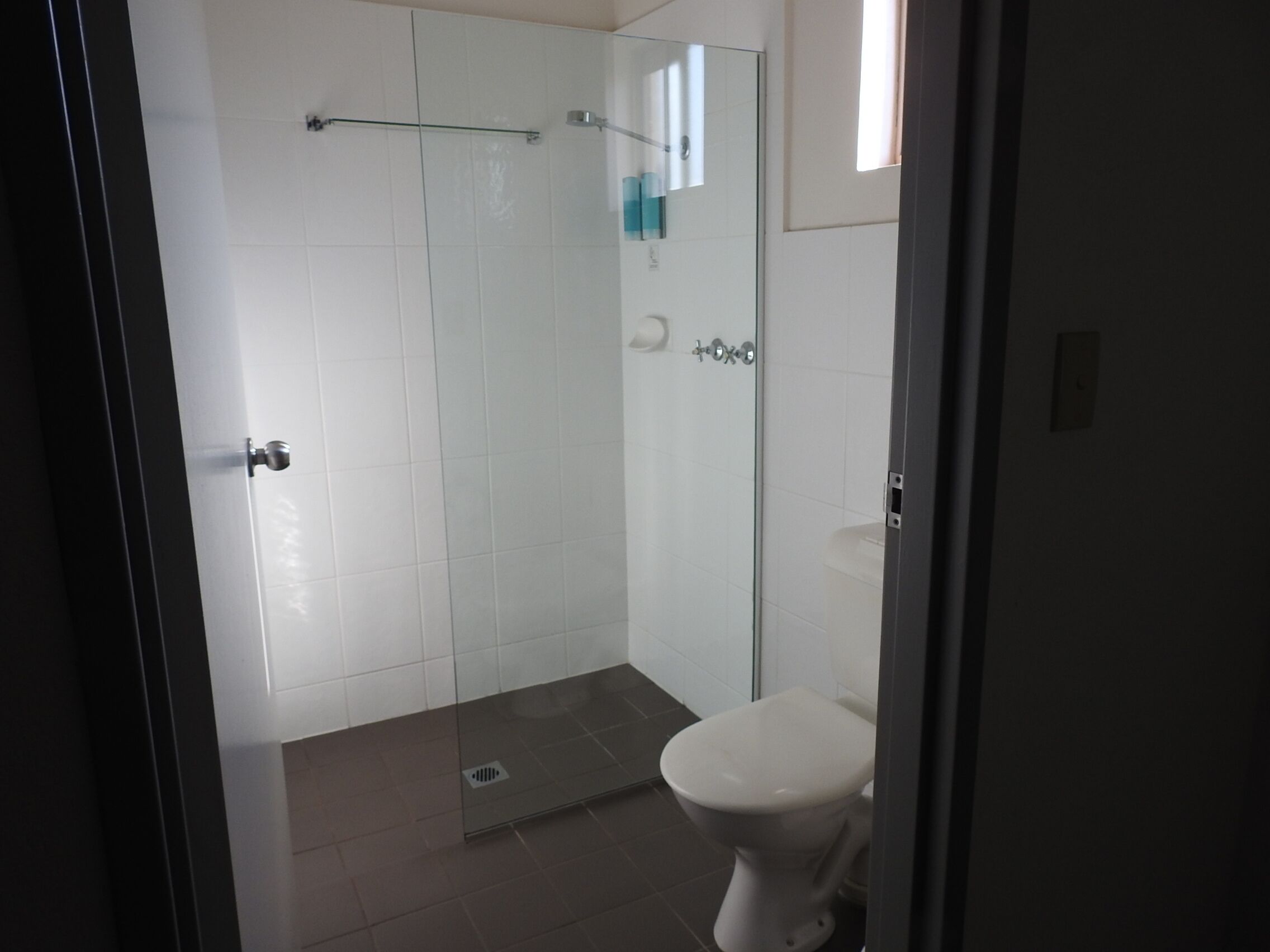 Baño con cabina de ducha de vidrio, inodoro y barra para toallas.