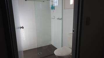 Baño con cabina de ducha de vidrio, inodoro y barra para toallas.
