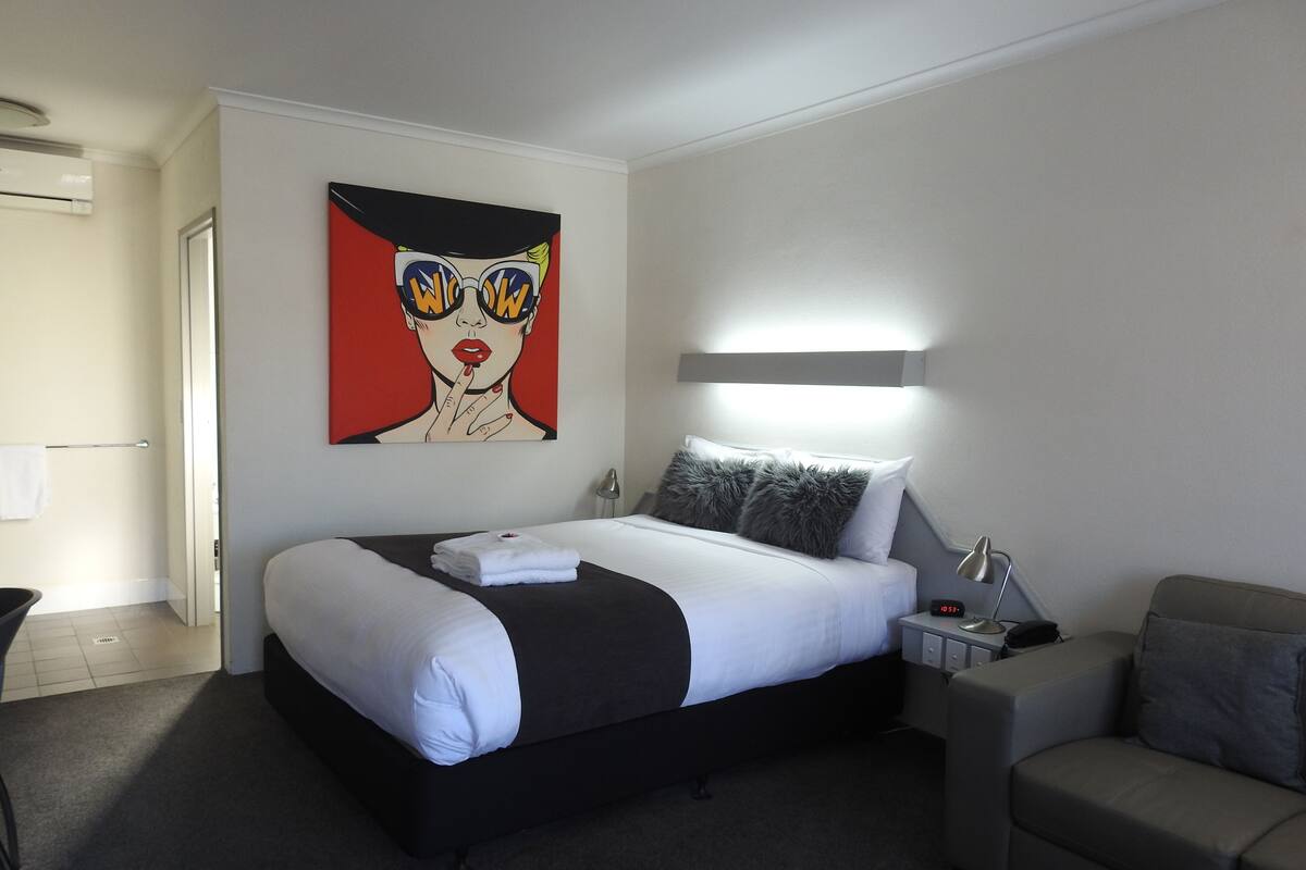 A hotel room with a bed, bedside table, lamp, and a painting on the wall.