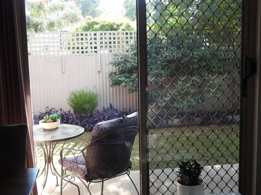 Un patio con una mesa y silla de metal, una cerca blanca y varias plantas.