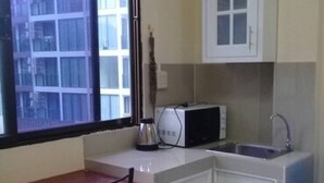 A compact kitchen with a window, a microwave, a sink, and a small dining table. - Hill Inn (Pattaya)