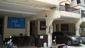 A hotel with a sign reading "Hill Inn," a parking area with a car and a scooter, and a staircase leading to the upper floor. - Hill Inn (Pattaya)