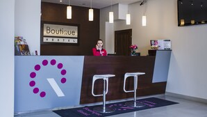 A hotel reception desk with a sign reading "Boutique Hostel," two bar stools, a reception area with a wooden counter, and a wall-mounted TV. - Boutique Hostel (Lodz)