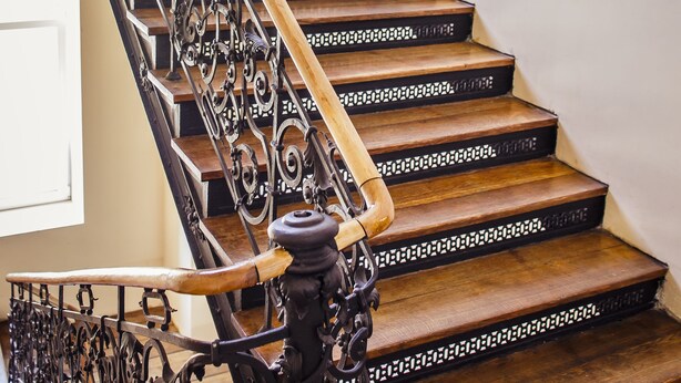 A wooden staircase with ornate black metal railings and a wooden handrail. - Boutique Hostel (Lodz)
