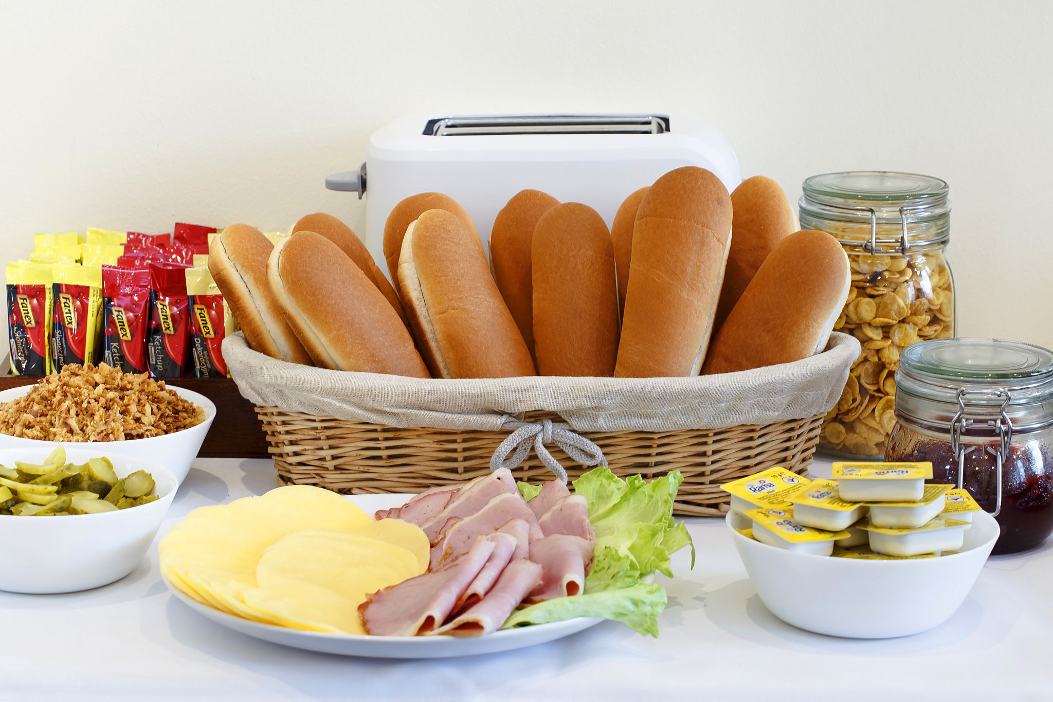 A table with various food items including bread, cheese, ham, pickles, and condiments.