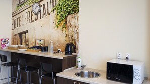 A kitchenette with a microwave, sink, and bar stools. - Boutique Hostel (Lodz)