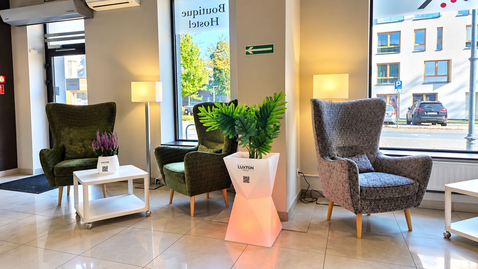 Un hall d’hôtel avec deux fauteuils verts, une table blanche et une plante posée sur un piédestal.