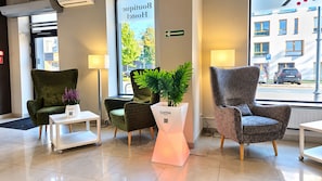 A hotel lobby with two green armchairs, a white table, and a plant on a pedestal. - Boutique Hostel (Lodz)