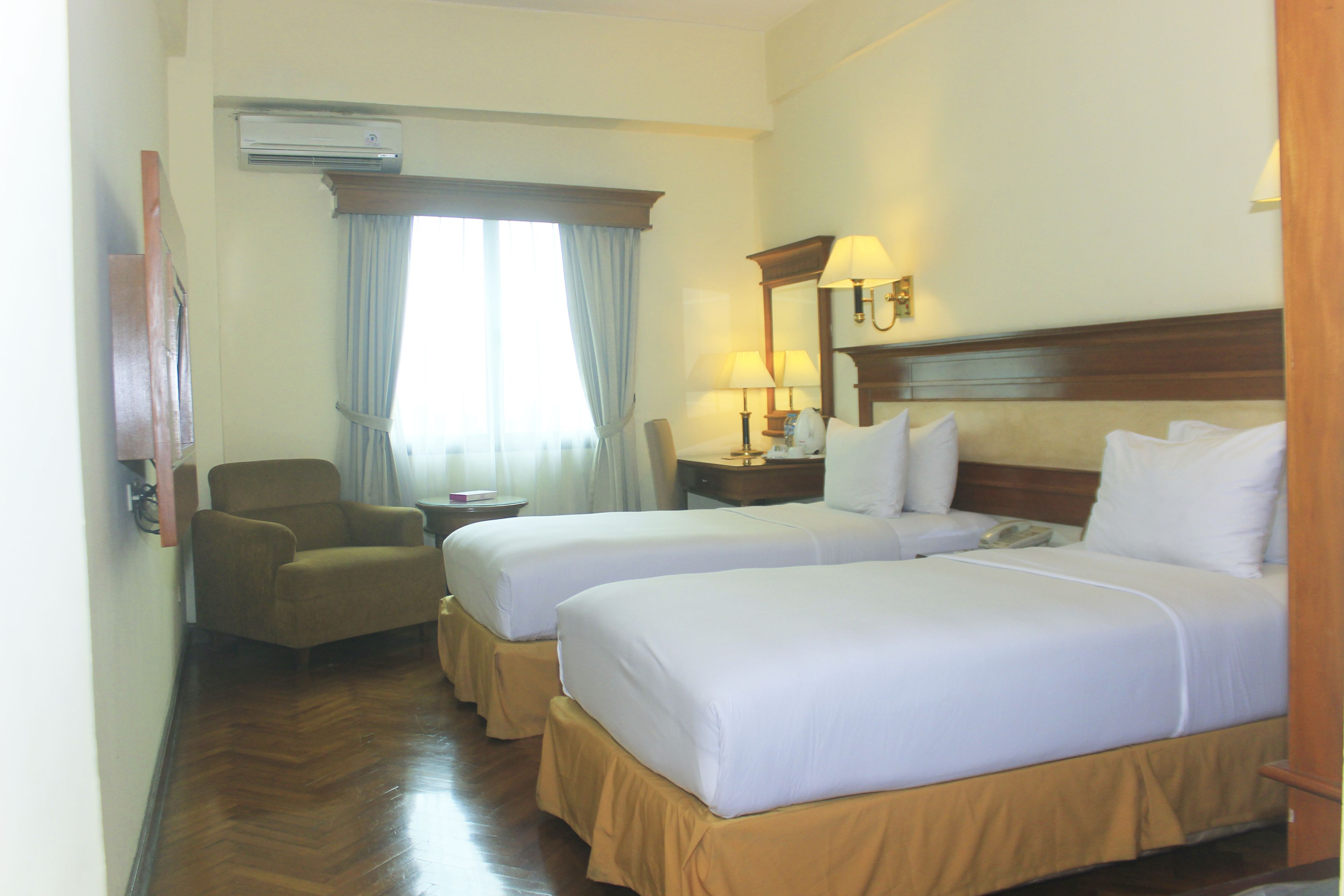 A hotel room with two beds, a chair, a desk, and a window with curtains.