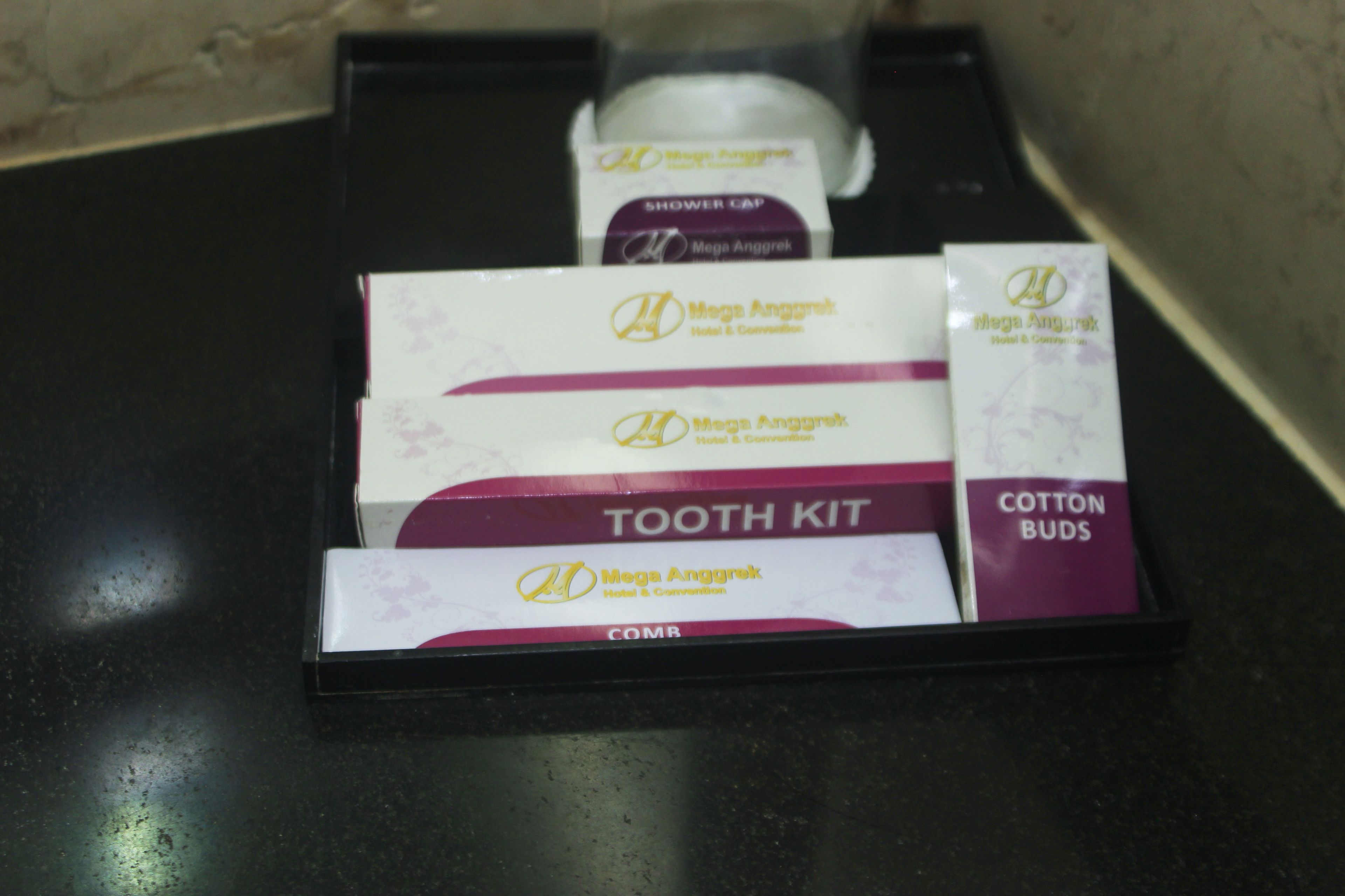 A black tray containing a Mega Anggrek Tooth Kit, Cotton Buds, and a Shower Cap.
