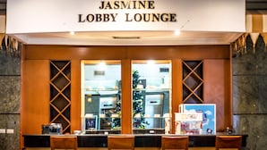 A lobby lounge with a sign reading "Jasmine Lobby Lounge". There are wooden chairs and tables in the seating area. A Christmas tree is visible through the window. - Mega Anggrek Hotel & Convention (Jakarta)