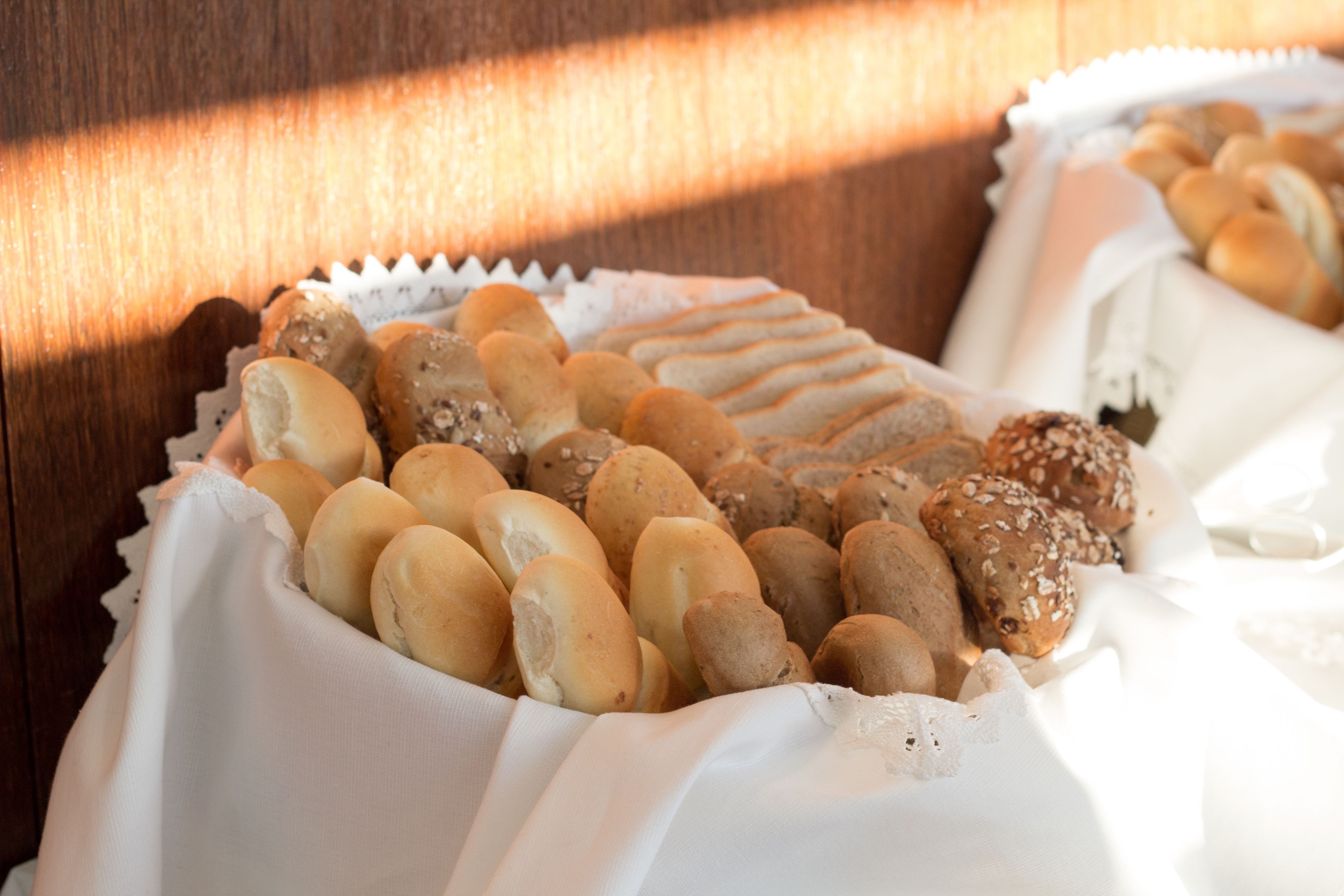A variety of breads and pastries arranged on a table with a white cloth, set against a wooden background.