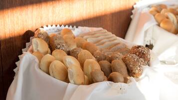 A variety of breads and pastries arranged on a table with a white cloth, set against a wooden background.
