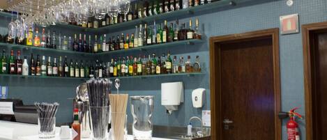 A bar area with shelves of liquor bottles, hanging glasses, and bar tools.