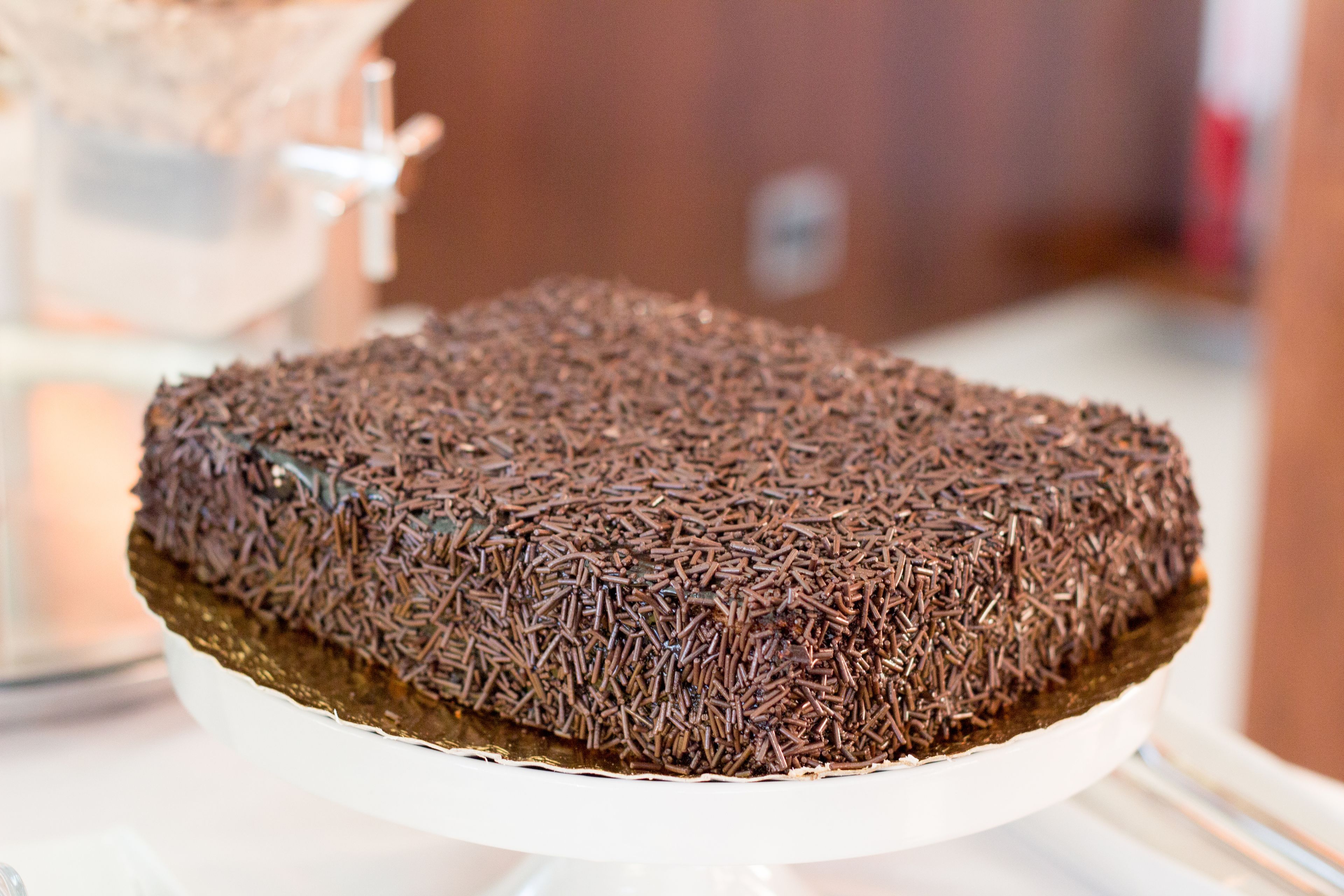 A chocolate cake with sprinkles on a white cake stand.