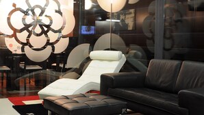 A modern lounge area with a black leather sofa, a white lounge chair, and a black and red rug. - Hotel Portas de Santa Rita (Valongo)