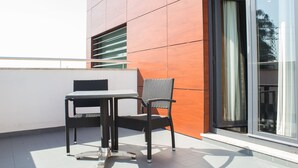 A balcony with a table and chair, a sliding glass door, and a modern building facade. - Hotel Portas de Santa Rita (Valongo)