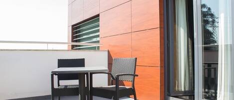 A balcony with a table and chair, a sliding glass door, and a modern building facade.