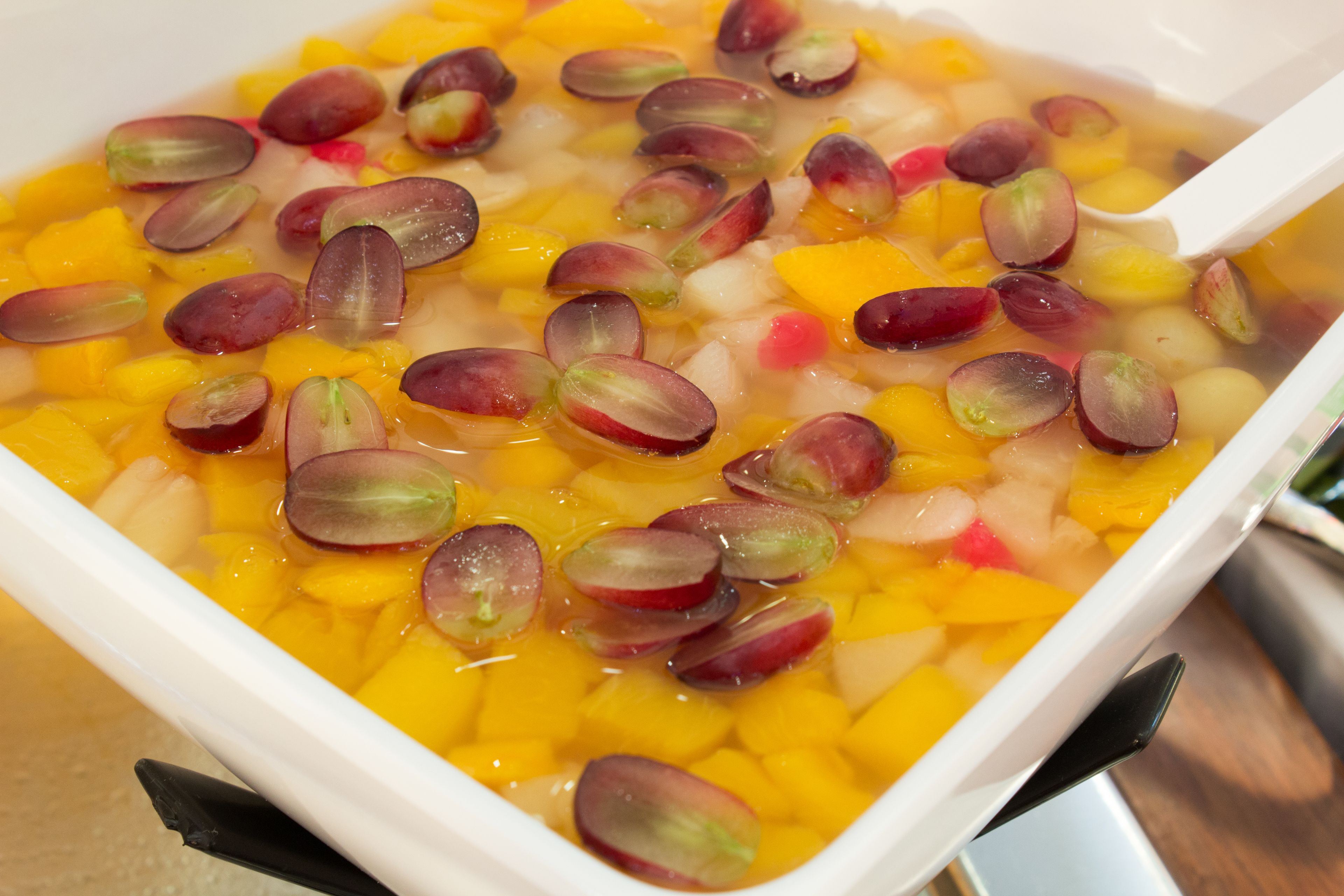 Un tazón de ensalada de frutas con trozos de mango y uvas rojas.