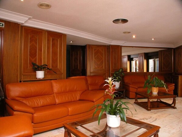 A living room with a leather sofa, a coffee table, and two potted plants. - Hotel Amefa (Salamanca)